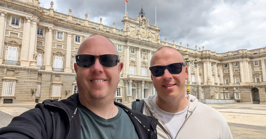 Kolyn & Denis of The Curious Tourists standing in front of the Royal Palace of Madrid in Spain