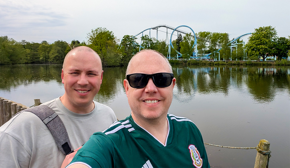 The Curious Tourists standing by the lake at Drayton Manor with The Wave roller coaster in the background